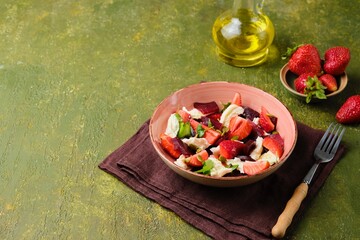 Healthy salad of boiled beets, mozzarella and fresh strawberries, dressed with olive oil and sprinkled with pumpkin seeds, in a pink ceramic plate on a green concrete background.