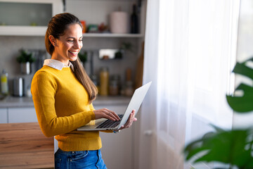 Smiling business woman using laptop computer while standing at home.