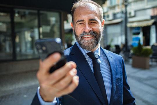 Smiling businessman in a suit holding a smartphone in city