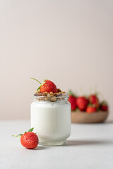 Natural yogurt in a glass jar with granola and strawberries on a light background with copy space
