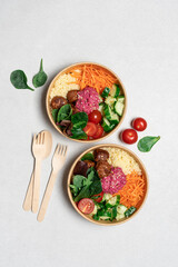 Healthy take away salad with vegan meatballs, vegetables, couscous and beetroot hummus  in disposable eco friendly paper containers on white background, top view