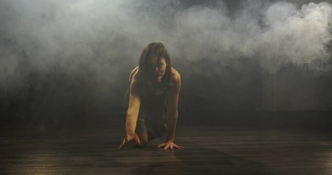 A young woman in a black sexy suit with belts and clasps on the bodice of the dress crawls along the floor
