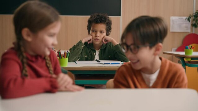 Two Caucasian children school lesson girl boy classmates laughing talk evil laugh mocking bully African American kid child schoolboy sad upset stressed lonely mock bullying kids class discrimination