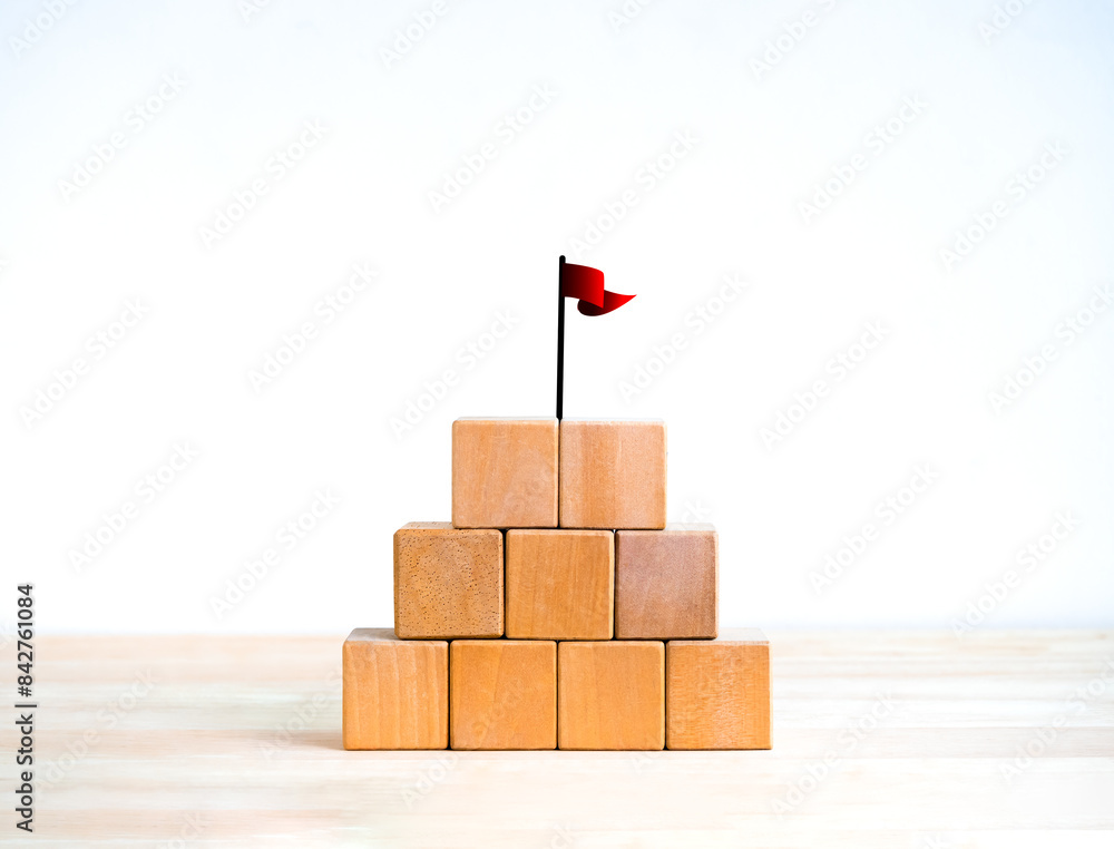 Poster red win flag on top of 5 wood blocks pyramid stack isolated on wooden table, white background. empty