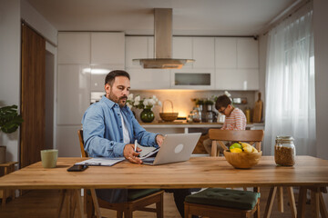 Adult man work form home on laptop with son at background