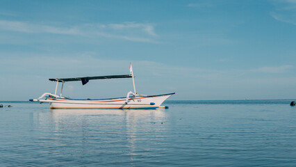 Obraz premium A fishing canoe idles in the middle of a calm sea under a blue sky.