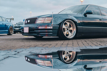 A modified old car is parked near a puddle at a Car Meet.