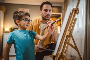 Father teach mentor son to create art at home on easel with brush