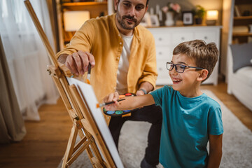 Father teach mentor son to create art at home on easel with brush