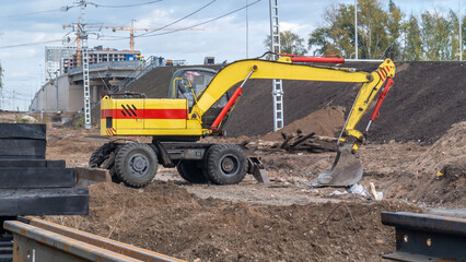 A yellow excavator at a construction site. A wheeled excavator for road construction. Equipment for digging trenches. Equipment for road and construction work.  Construction of roads and bridges.