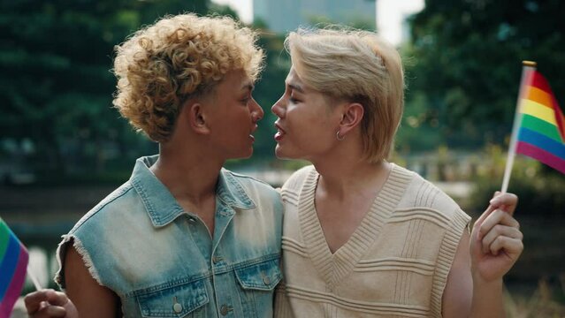 Smiling Gay Couple Holding LGBT Rainbow Flags in a Park, Celebrating Diversity and Pride. Both Wearing Casual Clothes and Radiating Joy