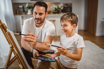 Fototapeta premium Father and son paint together at home learn and have fun bonding time