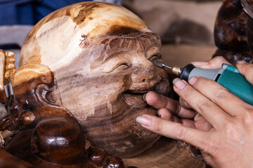 Close up of two hands holding a wood carving machine. They are carving the head of a buddha in a Vietnamese workshop.