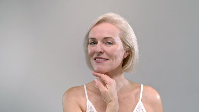 Portrait: beautiful old woman smiling and laughing in the studio. Middle aged senior female is flirting, healthy white teeth, smooth moisturized skin, blond hair. Concept of anti-aging skincare