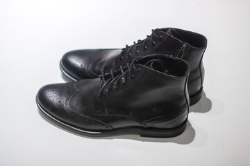 There are a pair of stylish black brogue boots placed on a clean white surface