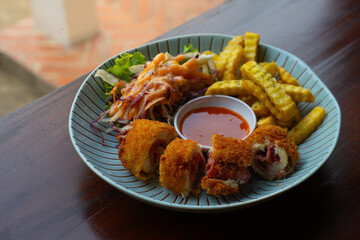 Chicken cordon bleu with crinkle cut fries and vegetable salad, served on striped blue plate, over wooden table, cafe environment