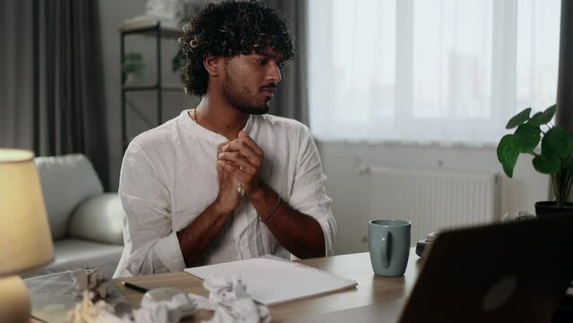 Sad young handsome indian man student or freelancer with lack of new ideas or creative block writing and crossed out at home workplace Worried male with failed ideas working or studying indoors