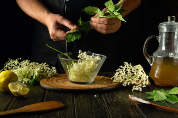 Adding green mint by hand to a glass bowl with elderberries before making a cold drink or kvass....