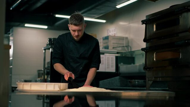 in a professional kitchen in a pizzeria young chef in a black uniform prepares pizza dough