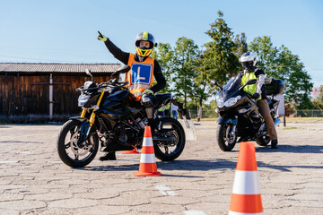 Two motorcyclists with L sign are stopped at auto drome. One of them is pointing to the other.