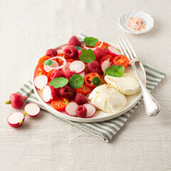 Summer salad with raspberries, cherry tomatoes, fresh radishes, mozzarella cheese and nasturtium leaves. Berries in salads, fruit salty dishes. So French. Natural cotton, farm products, summer vibes