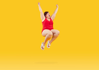 Fat woman having fun on summer holiday and jumping in ocean water on beach. Funny happy excited thrilled scared young overweight girl in red swimsuit screams as she jumps isolated on yellow background