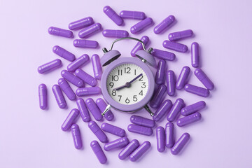 Sleeping pill concept with capsules and alarm clock on purple background