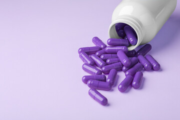 Purple pill capsules spilling out of drug bottle on purple background
