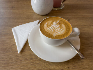 filiżanka świeżo parzonej kawy z pianką mleczną i wzorkiem, stojąca na stoliku w kawiarni © Kamil_k2p