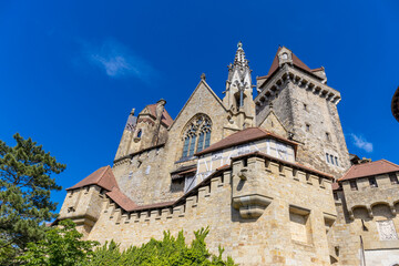 Fototapeta premium Castle landmark under blue sky. Medieval castle in Austria. Ancient historical sights around Vienna. Castle Kreuzenstein old building from outside