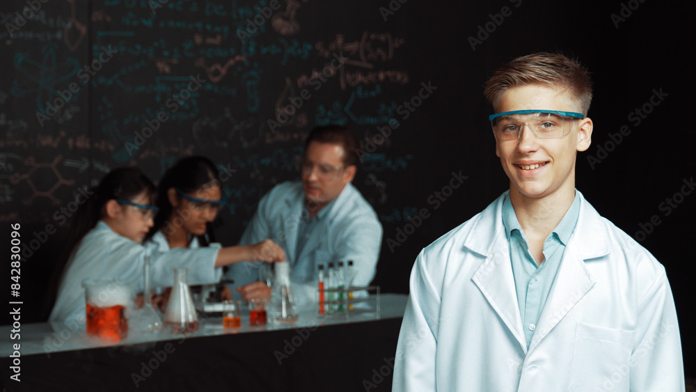 Poster smart student looking at camera while diverse group doing experiment. attractive academic boy standi