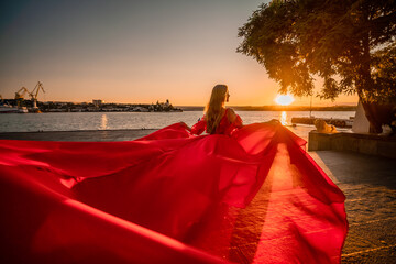 Sunrise red dress. A woman in a long red dress against the backdrop of sunrise, bright golden light...