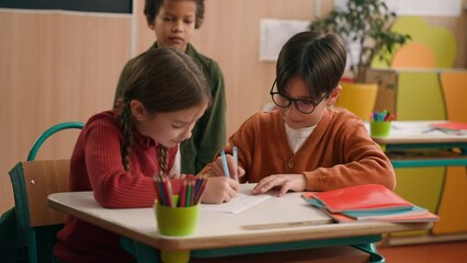 Two Caucasian children school lesson girl boy classmates drawing writing in notebooks African American kid child schoolboy approach look at picture dissatisfied mock talking pointing bullying go away