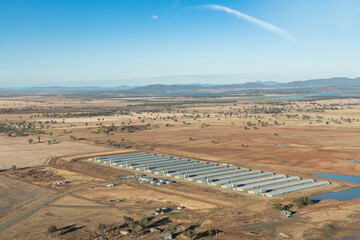 Close up aerial view of rows of industrial factory farmed chicken sheds closed buildings with artificial light and ventilation set in empty overgrazed landscape