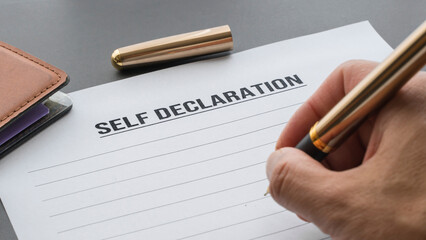 hand holding a pen ready to write a self-declaration