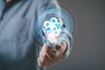 businessman Hand holding smart phone and light bulb with gear glowing with orange light and ray. Creative and new business knowledge thinking idea concept.	
