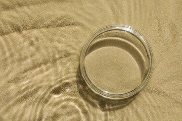 Stylish presentation for product. Glass podium in water on sand, top view. Space for text