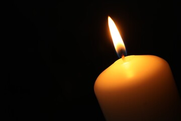 One burning church candle on black background, closeup. Space for text