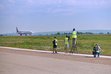 Photographers at the airfield prepare to photograph an airliner taking off. Spotting on a sunny summer day. Selective focus.