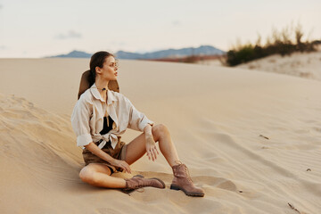Lonely woman sitting on sand dune in the middle of desert under clear blue sky