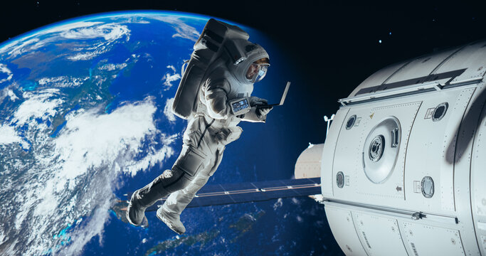 Male Astronaut Using Laptop to Wirelessly Connect to a Satellite. Spaceman Working on a Device in Open Space Outside Earth Atmosphere. Professional Engineer Undertaking Service and Maintenance Job