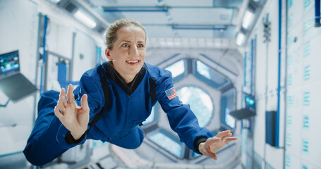 Female Astronaut Floating in International Space Station, Wearing Blue Spacesuit, Smiling....