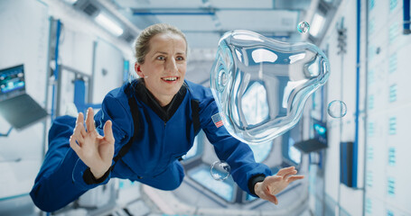 Female Astronaut in Blue Spacesuit Floating Inside Space Station, Interacting with Floating Water Bubble. Demonstrates Human Achievement in Space Exploration. Cosmos Encourages  Scientific Discovery