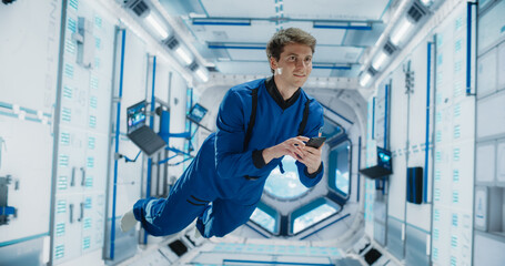 Male Astronaut Floating in Zero Gravity Inside a Space Station. Spaceman Using a Smartphone in Space in Orbiting Spacecraft, Browsing Internet Content and checking and Updating Social Media Networks.