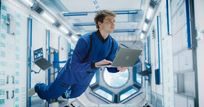 Male Astronaut Using a Laptop to Wirelessly Connect to a Satellite. Space Scientist Working on Computer Device Inside an Intergalactic Station. Professional Engineer Undertaking Online Service Job