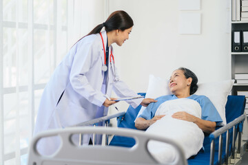 Doctor woman in a white coat is talking to an older woman in a hospital bed