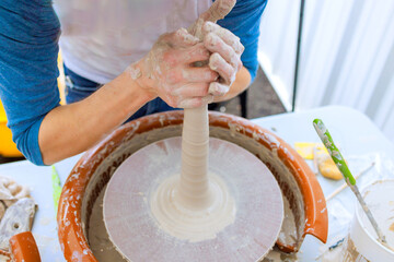 Clay dishes are crafted by potter who is hand sculpting soft clay with wet hands as he turns it on wheel