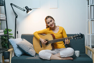 Asian woman is sitting on a couch playing a guitar