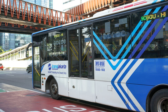 A blue Transjakarta bus that is stopped in front of the bus stop is dropping, picking up and transporting passengers during office rush hour and traffic jam. Green. Jakarta, Indonesia.