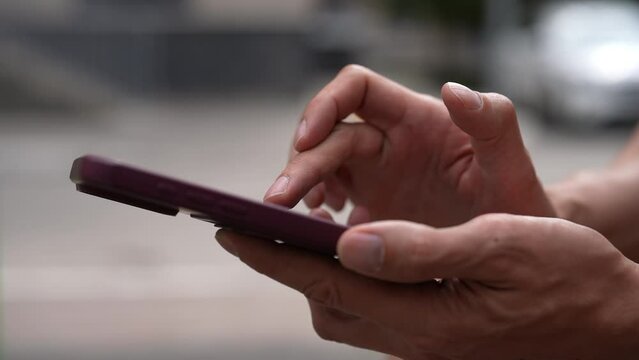 Side view of man clicking smartphone screen to farming new popular Hamster Kombat cryptocurrency in mobile phone online application. Male extract crypto coins using smartphone outdoors, slow motion.